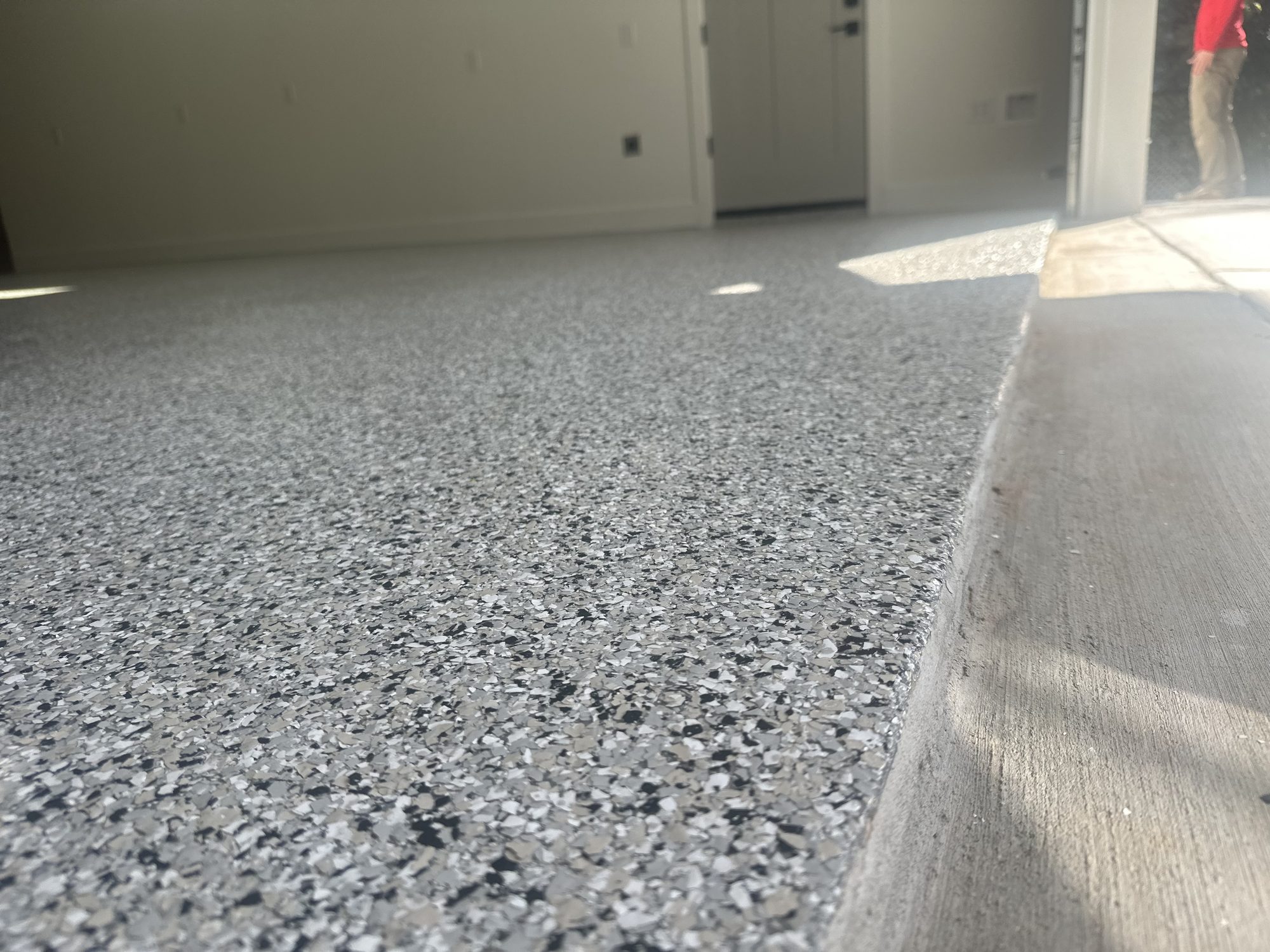 Gray and black flake epoxy garage floor, camera low at the slab edge, open garage door beyond, Huntsville, AL
