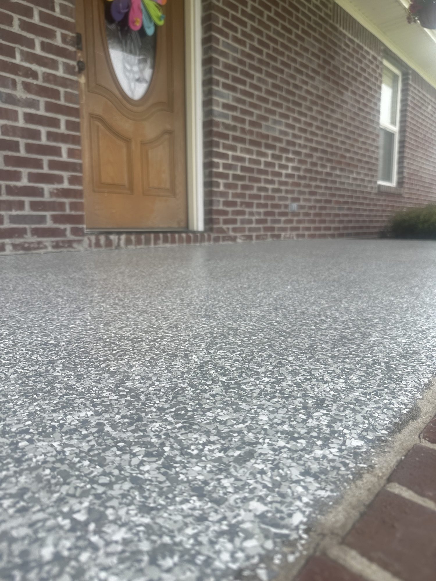 Gray and white flake epoxy porch floor at a brick house with a wooden front door, Huntsville, AL