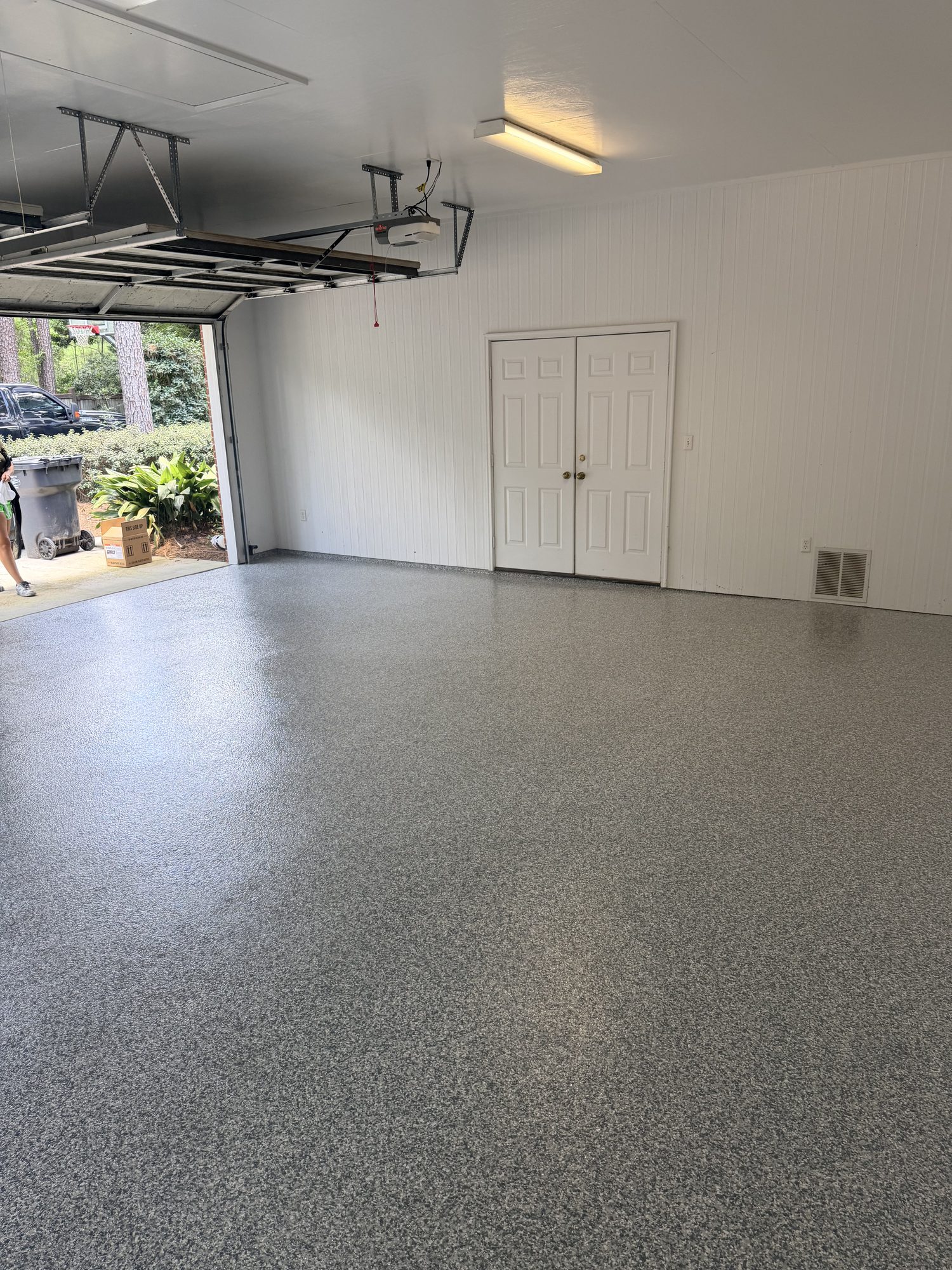 Gray flake epoxy garage floor with overhead storage racks and a white double door, Huntsville, AL