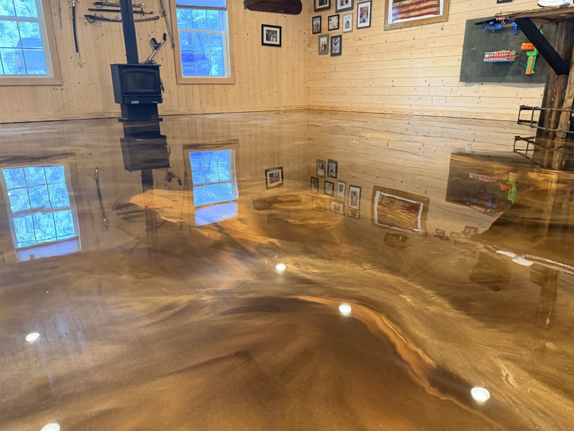 Copper and bronze metallic epoxy floor in a pine walled cabin room, reflecting the wood stove and windows, Huntsville, AL