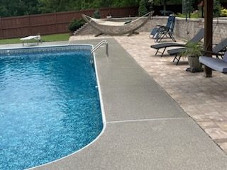 Concrete pool deck curving around a pool edge, pavers and loungers beyond, Huntsville, AL
