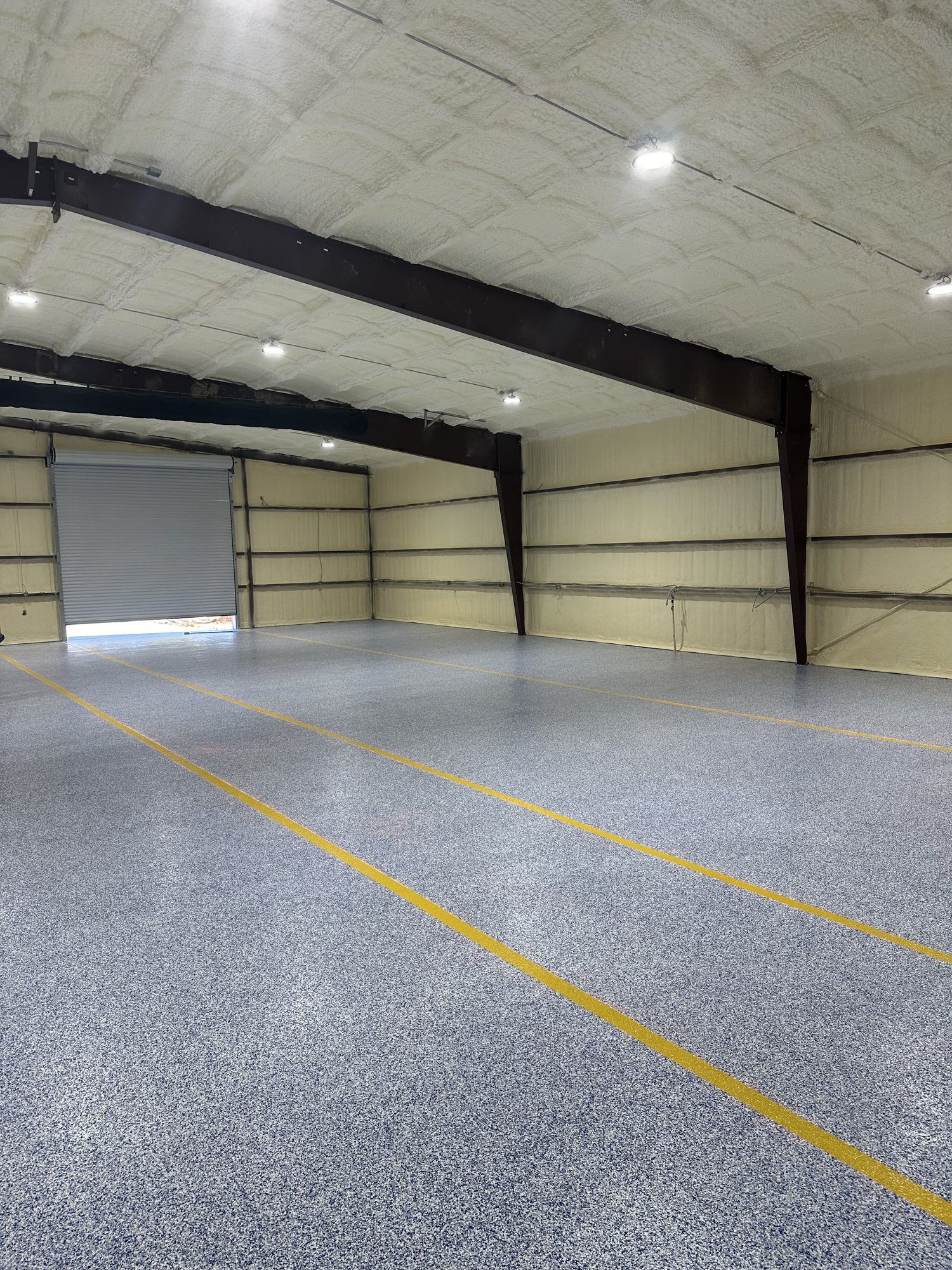 Gray flake epoxy warehouse floor with yellow striping under steel beams, Huntsville, AL