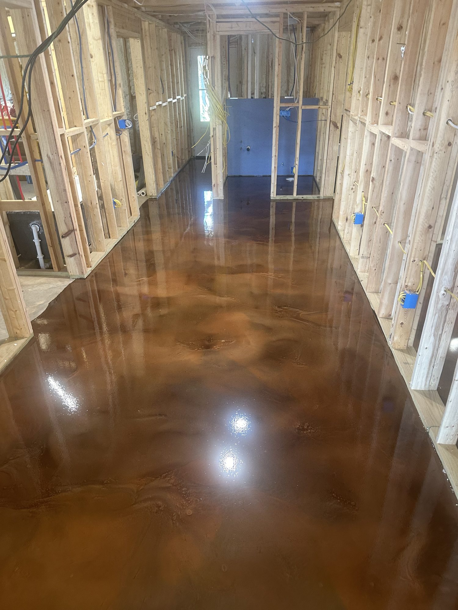 Rust brown metallic epoxy floor running down a corridor framed by exposed stud walls, Huntsville, AL