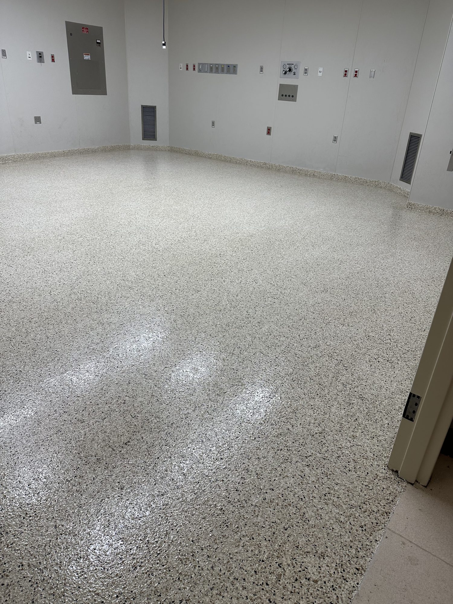 Pale polished concrete floor with exposed stone aggregate against a white wall, Huntsville, AL