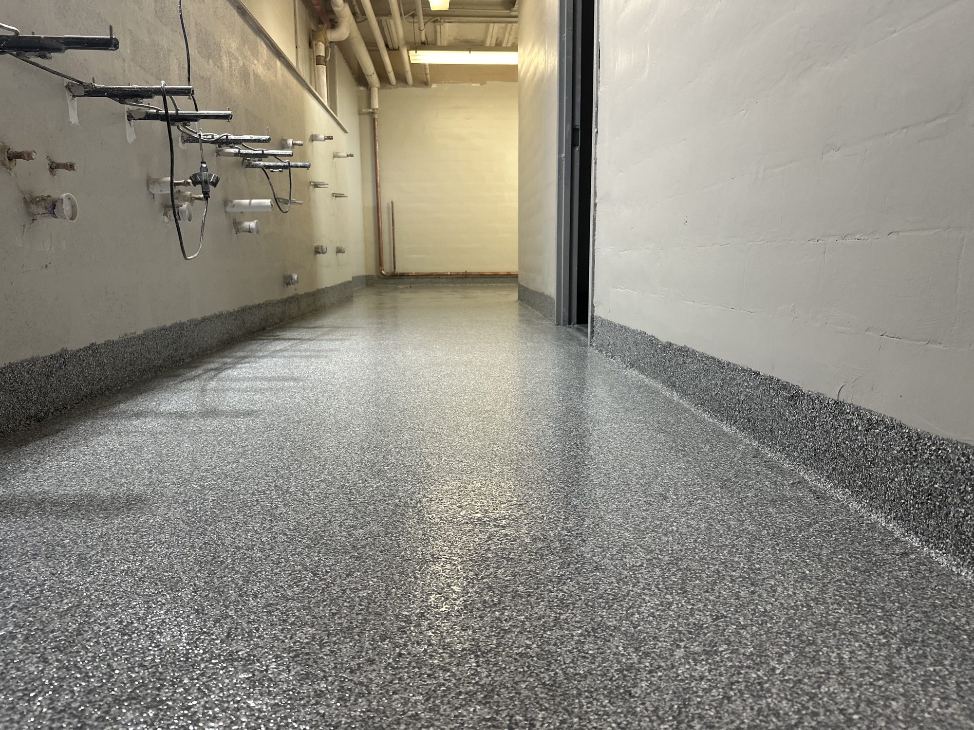 Gray flake epoxy floor with cove base in a utility corridor, pipework on the wall, Huntsville, AL